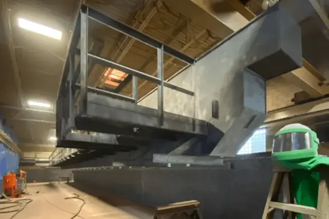 Large steel structure surface preparation — operator in full blast suit