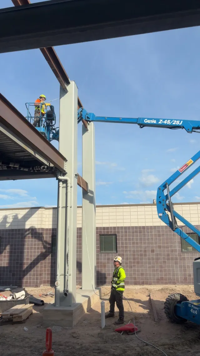 Crew priming structural steel column on boom lift — new construction Taylor MI
